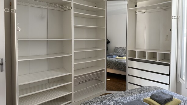 A bedroom with a bed, a wardrobe, and a closet with multiple shelves.