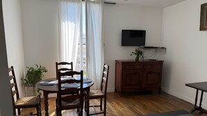 A room with a dining table, chairs, a television, a cabinet, and a sofa.