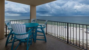 Een balkon met stoelen en een tafel, met uitzicht op een strand met parasols en mensen.