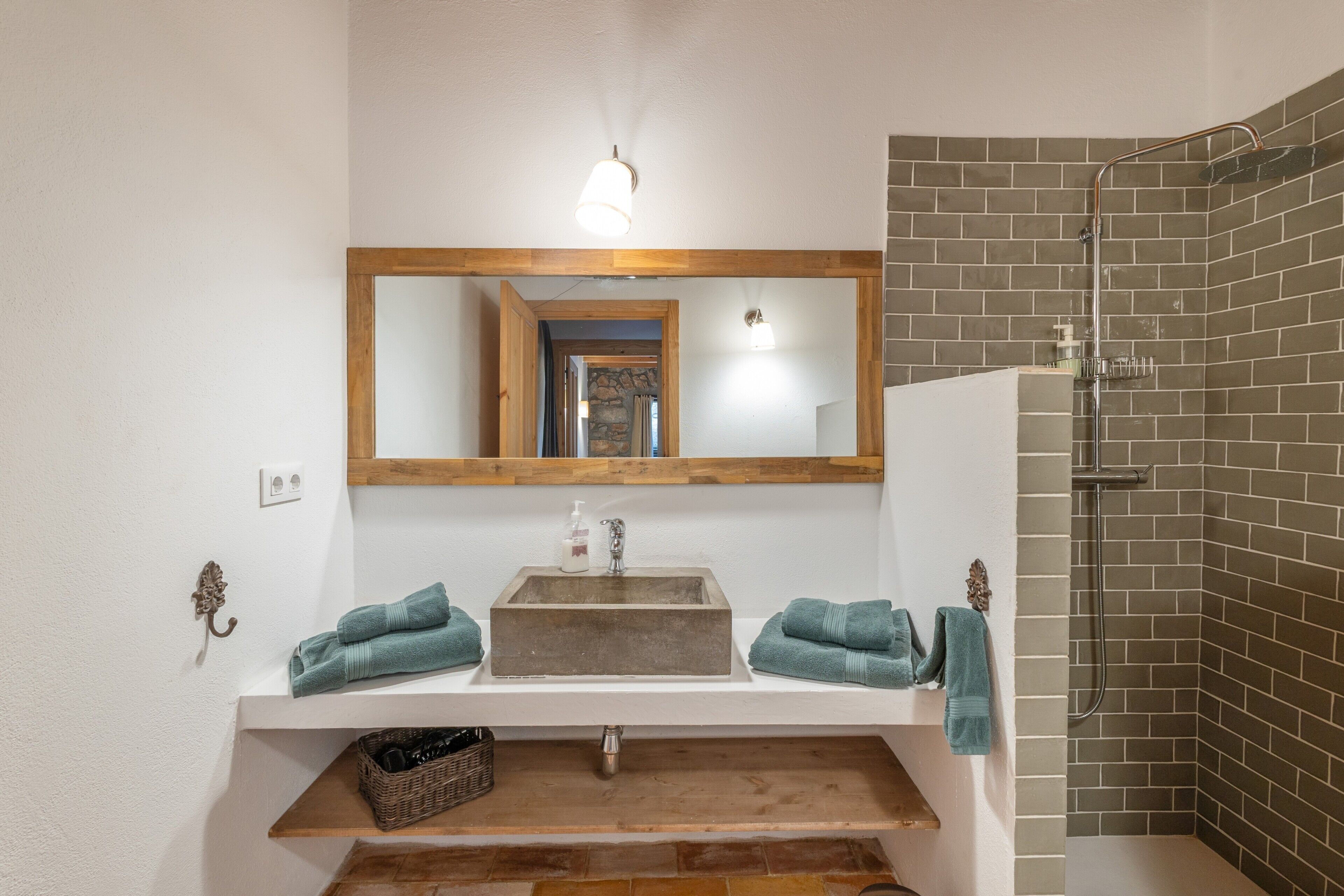 Un baño con tocador de madera, un espejo grande, ducha con pared de ladrillo y toallero colgante.