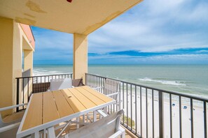 A balcony with a wooden table and chairs, overlooking a beach with the ocean and a clear sky. - Phoenix V 1516 2 Bedroom Condo (Orange Beach)