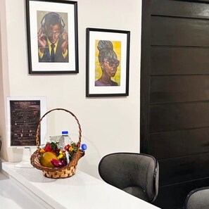 Un comptoir d’accueil orné d’œuvres d’art encadrées, un panier rempli de fruits et une bouteille, ainsi qu’une chaise noire.