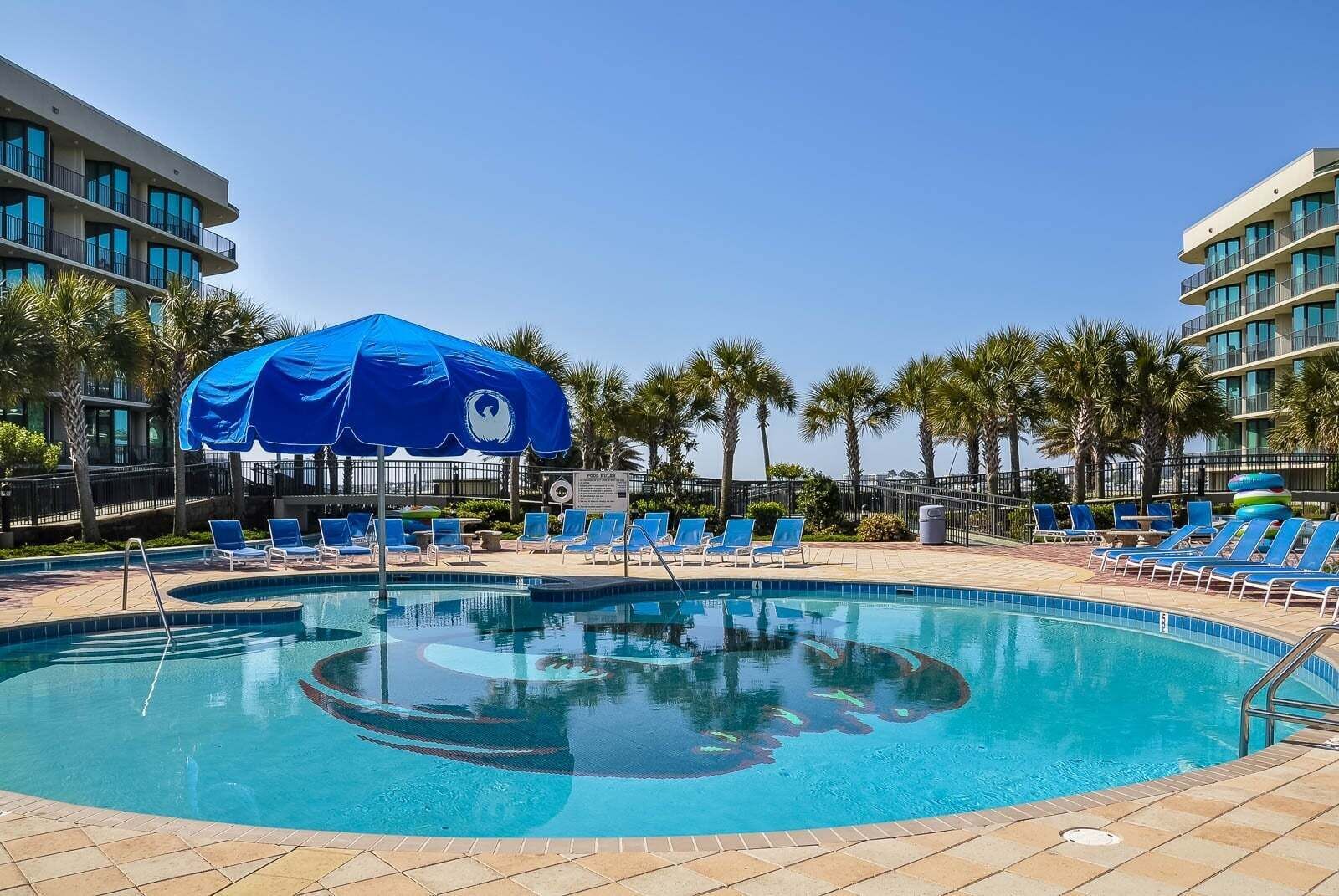 Una piscina con sillas reclinables azules y una sombrilla azul.