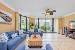 A spacious living room with a large sofa set, a coffee table, a television, and a ceiling fan. - Phoenix On The Bay 1211 3 Bedroom Condo (Orange Beach)
