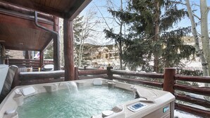A hot tub with a control panel, surrounded by a wooden deck and a metal railing, with snow-covered ground and trees in the background. - Deer Valley Condo Near Base Hot Tub (Park City)