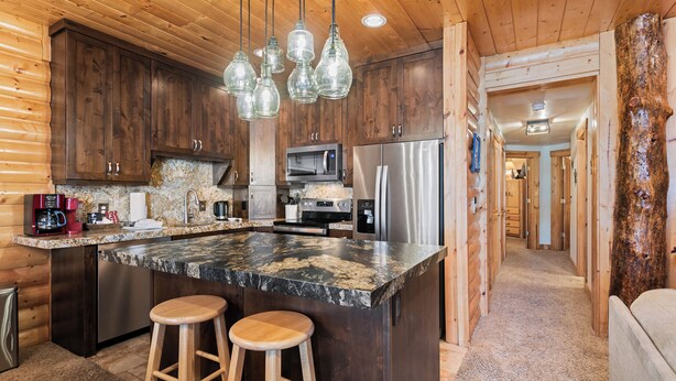 A kitchen with wooden cabinets, a granite countertop, stainless steel appliances, and hanging pendant lights. - Deer Valley Condo Near Base Hot Tub (Park City)