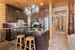 A kitchen with wooden cabinets, a granite countertop, stainless steel appliances, and hanging pendant lights. - Deer Valley Condo Near Base Hot Tub (Park City)