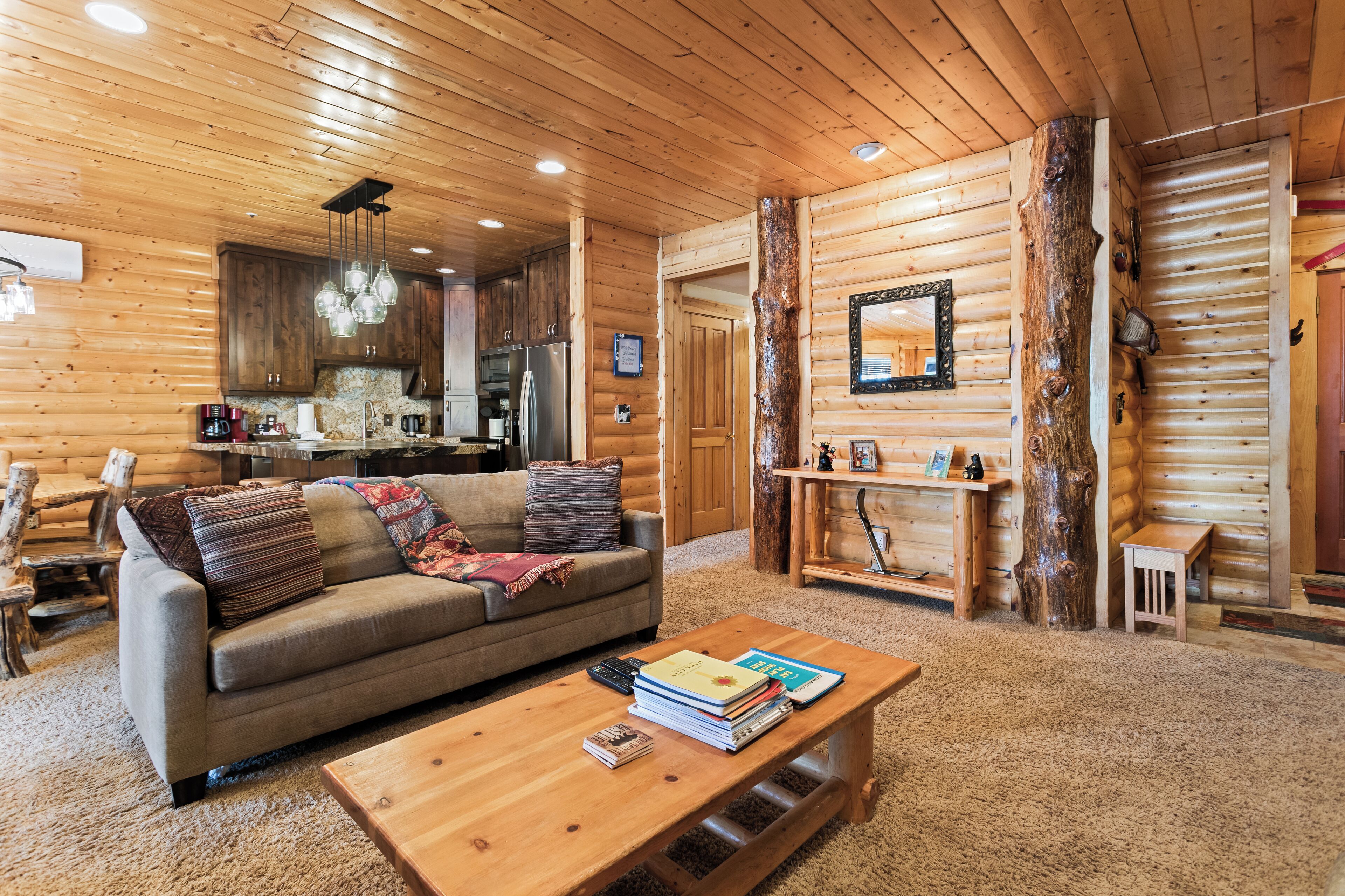 A log cabin interior with a sofa, coffee table, wooden walls, and a kitchen area.