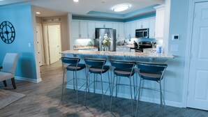 A modern kitchen with a central island, bar stools, and a clock on the wall. - 705 Margate, 3 bedroom ocean front condo 3 Condo (Myrtle Beach)