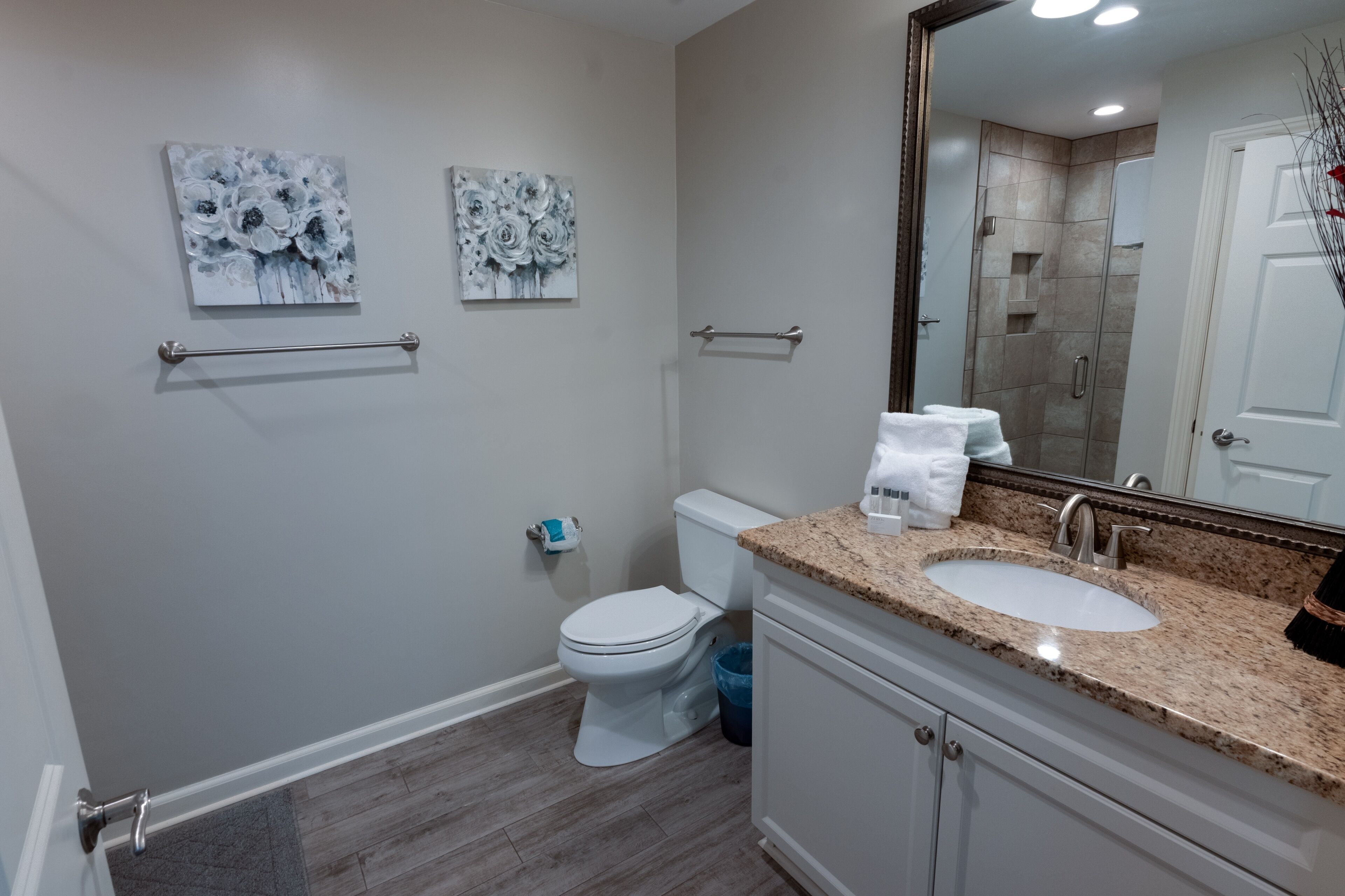 Un baño con inodoro blanco, un lavamanos con encimera de granito y dos toalleros de pared.