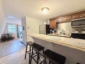 A kitchen with a large island, wooden cabinets, a refrigerator, and a microwave. There are two stools at the island. - A Frame Escape Lake Access (Rocky Mount)