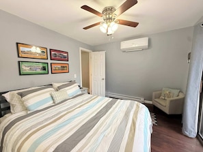 A bedroom with a bed, a ceiling fan, wall-mounted air conditioning, framed pictures, and a door. - A Frame Escape Lake Access (Rocky Mount)