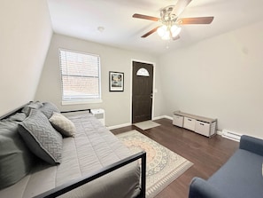 A bedroom with a bed, a ceiling fan, a window with blinds, a door, and a small rug. - A Frame Escape Lake Access (Rocky Mount)