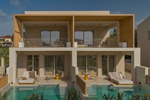 Un bâtiment moderne à deux étages doté d’une piscine, de balcons et d’un espace extérieur aménagé pour s’asseoir.
