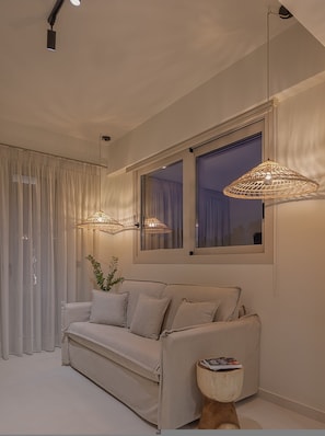 Un salon moderne avec un canapé, deux lampes suspendues, une fenêtre avec des rideaux et une petite table d’appoint en bois.