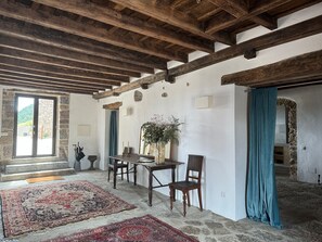 Una habitación rústica con paredes de piedra, vigas de madera, una mesa de comedor con sillas, una alfombra grande y una planta en maceta.