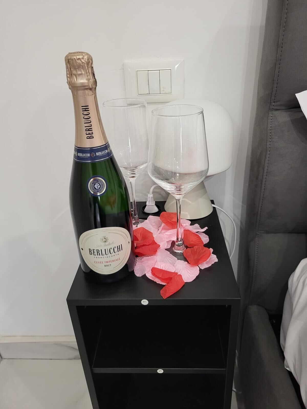 A bottle of Berlucchi champagne, two glasses, and a small table with a pink cloth.