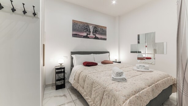 A modern bedroom with a bed, a nightstand, a wall-mounted mirror, and a painting. - Rome in Love Caffarella - Metro P. Lungo (Rome)