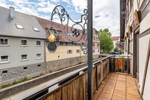A balcony with a wooden floor, a metal gate, and a building with a tiled roof and a yellow wall. - Vacation at the Winery – Apartment "Kleine Galerie" (Königheim)