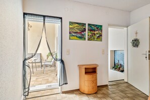 A room with a sliding glass door, a wooden side table, and two abstract paintings on the wall. - Vacation at the Winery – Apartment "Kleine Galerie" (Königheim)