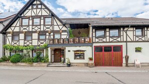 Ein traditionelles Fachwerkhäuschen mit einem markanten Eingang, einer roten Garagentür und einem kleinen Garten mit Kübelpflanzen.