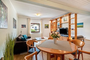 Una sala de estar moderna con un sofá, una mesa de comedor, sillas, un televisor y una estantería.
