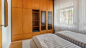 Ein Schlafzimmer mit einem Holzschrank, einem Bett mit gestreifter Bettwäsche und einem Fenster mit transparenten Vorhängen.