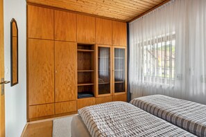 A bedroom with a wooden wardrobe, a bed with striped bedding, and a window with sheer curtains. - Vacation at the Winery – Apartment "Kleine Galerie" (Königheim)