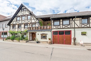 A traditional half-timbered building with a red door, a balcony, and a small shop window. - Vacation at the Winery – Apartment "Kleine Galerie" (Königheim)
