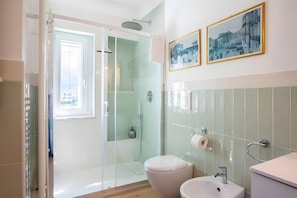 Un bagno moderno con box doccia in vetro, un water, un lavandino e due quadri appesi alla parete.