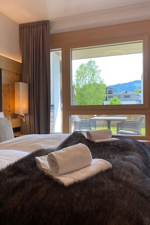 A hotel room with a bed, a large window, a view of the outdoors, and a wooden headboard. - 3_SPA - Deluxe Garden 413 by Interhome (Zell am See)