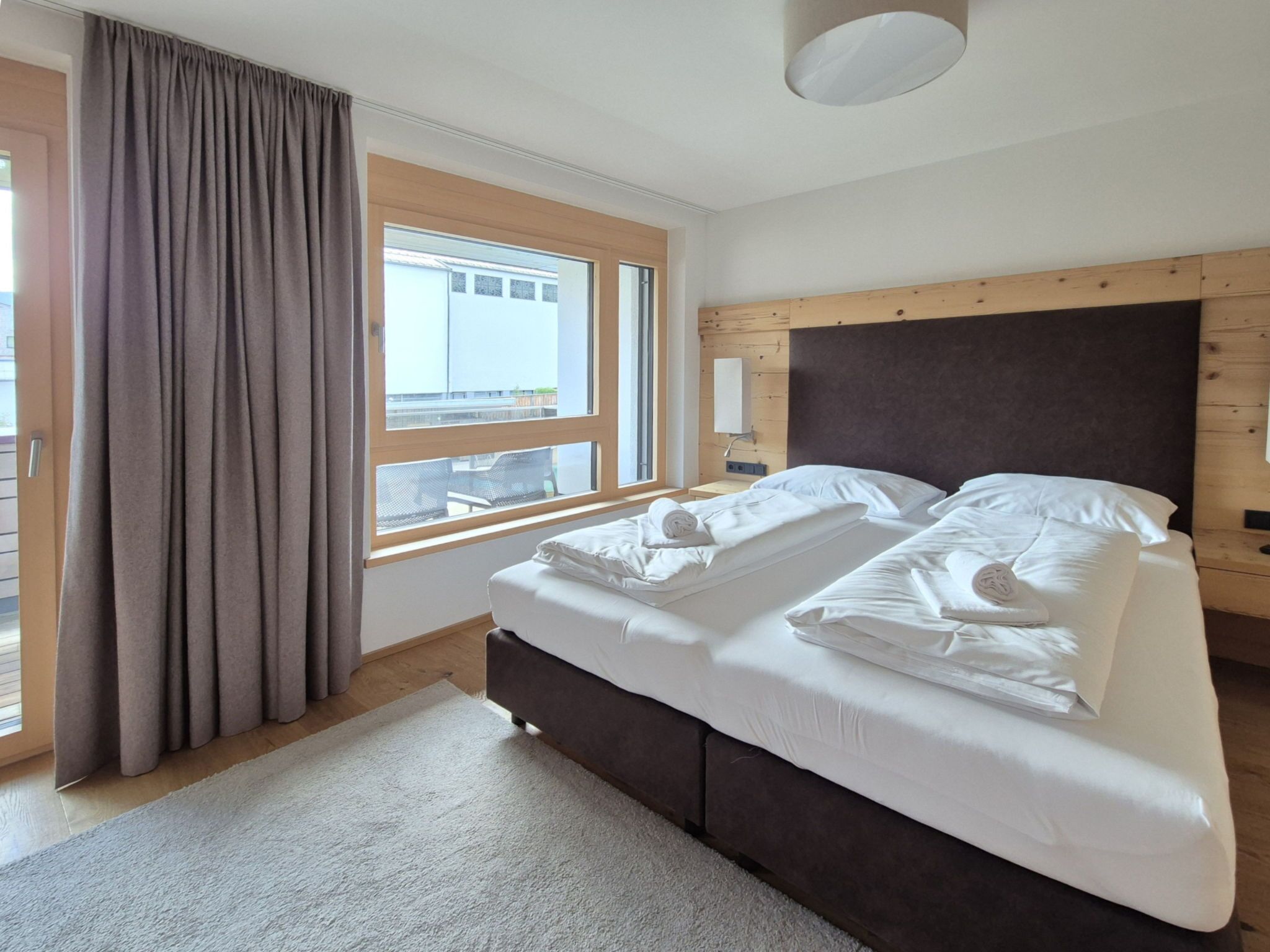 A bedroom with a bed, a window, curtains, and a wooden headboard.