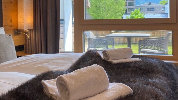 Une chambre d’hôtel avec un lit, une grande fenêtre, une vue sur l’extérieur et une tête de lit en bois.