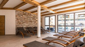 Habitación soleada con vigas de madera, pared de piedra y varios sillones de descanso.