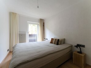 Un dormitorio con cama, lámpara de noche, ventana con cortinas y radiador.