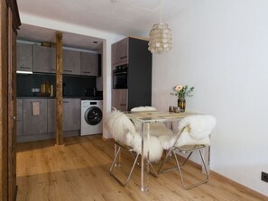 Una cocina moderna con armarios grises, lavadora y comedor con mesa de vidrio y sillas blancas de aspecto mullido.