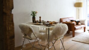 Ein Essbereich mit einem Tisch für zwei Personen, einer Blumenvase und einer Couch im Hintergrund.