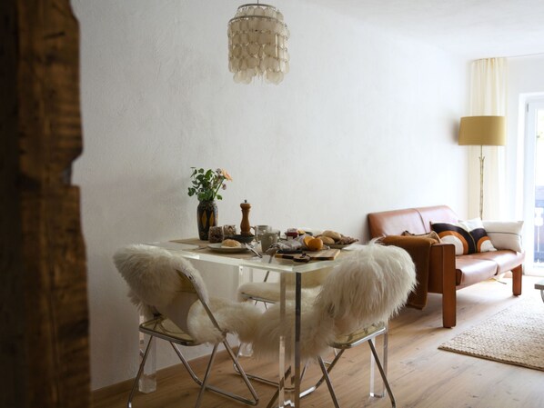 Un comedor con una mesa dispuesta para dos personas, un florero con flores y un sofá al fondo.