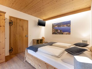 Un dormitorio con una cama de madera, televisor, un cuadro de un lago y un armario de madera.