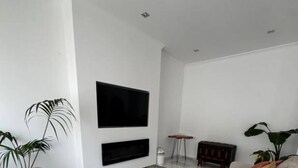 Een moderne woonkamer met een bank, een glazen salontafel, een aan de muur bevestigde televisie en een klein bijzettafeltje.