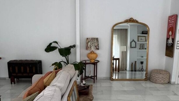 Een woonkamer met een bank, een spiegel, een lamp en een plant.