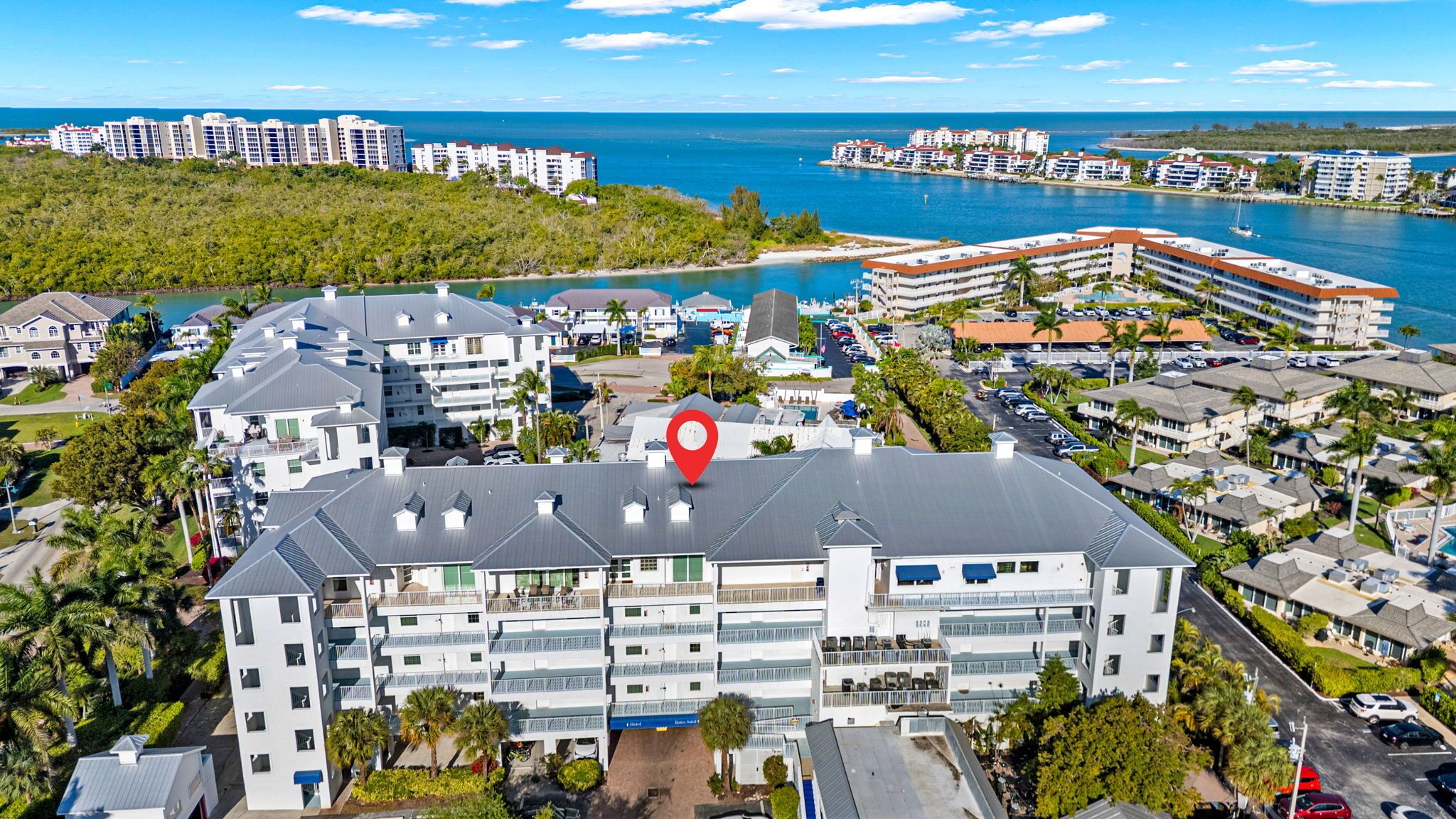 Ein mehrstöckiges Hotel mit einem zentralen Innenhof, umgeben von üppigem Grün und Blick auf das Meer.