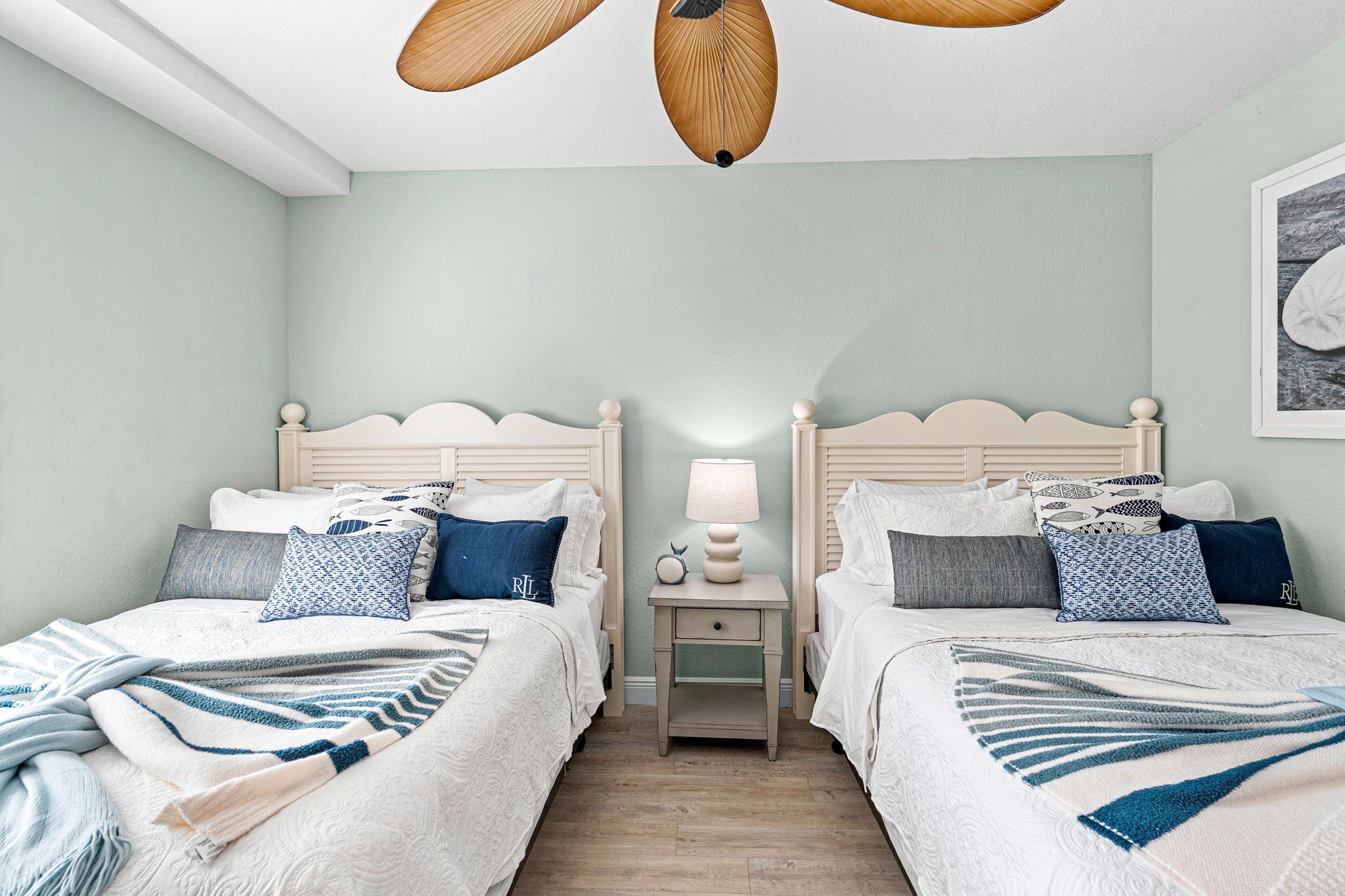 Un dormitorio con dos camas, una mesita de noche con lámpara y un ventilador de techo.