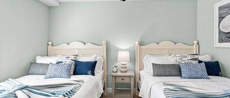 Un dormitorio con dos camas, una mesita de noche con lámpara y un ventilador de techo.
