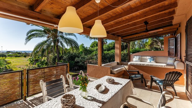 A covered outdoor area with a wooden ceiling, two pendant lights, a table with chairs, a grill, and a view of the landscape. - Villa Simonetta with Sea View, Wi-Fi, and Air Conditioning (Costa Rei)