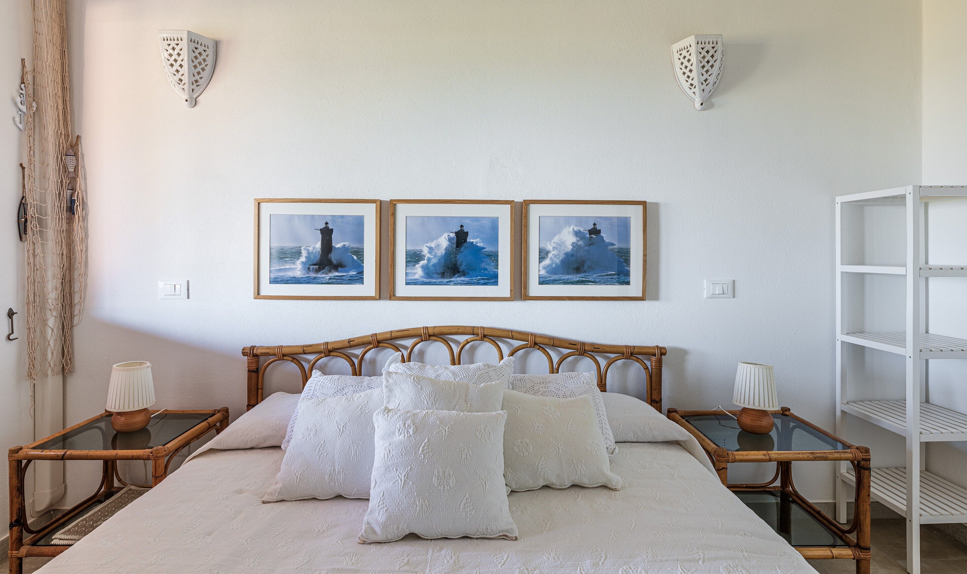 A bed with white linens, a wooden headboard, and three framed pictures of a lighthouse on the wall.