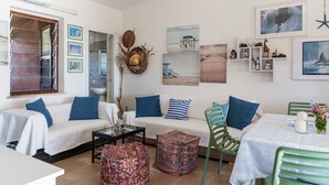 A living room with a sofa, ottoman, and a table with a candle and flowers. - Villa Simonetta with Sea View, Wi-Fi, and Air Conditioning (Costa Rei)