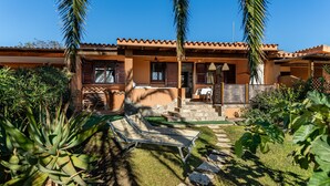 A two-story building with a tiled roof, a patio with a table and chairs, and a small garden area with plants and a sun lounger. - Villa Simonetta with Sea View, Wi-Fi, and Air Conditioning (Costa Rei)