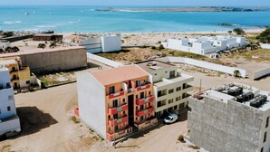Zona residencial costeira com edifícios, praia e barcos ao longe.