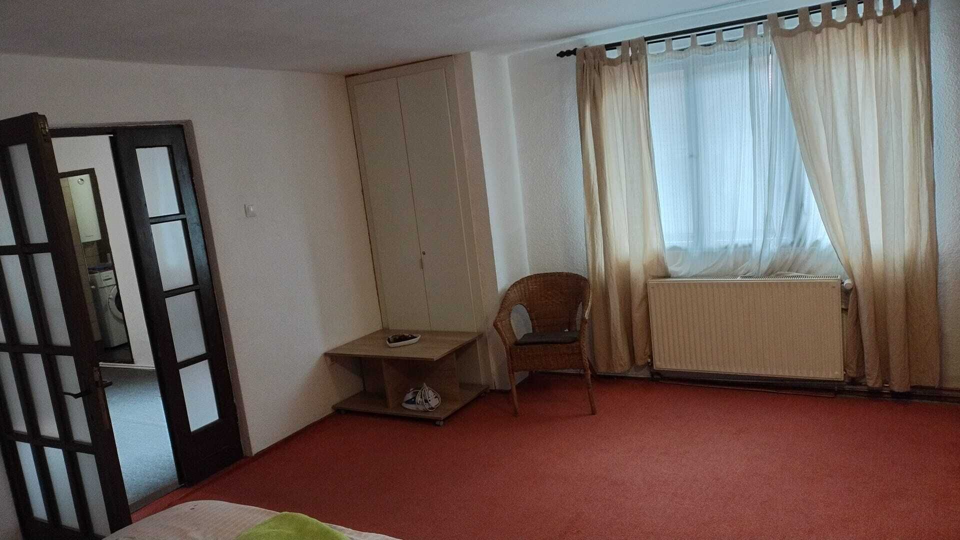 A room with a bed, a chair, a radiator, a window with curtains, and a wardrobe.